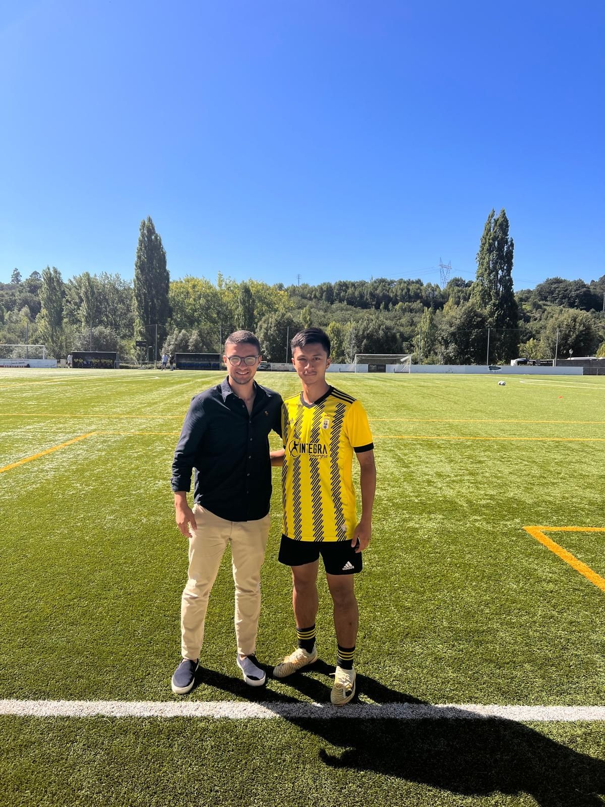 Two people standing on a sunny soccer field with trees and blue sky in the background.