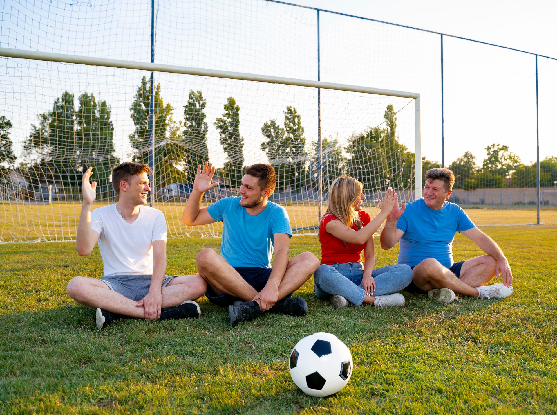 Group of Caucasian people deferent ages,  sitting on soccer field, giving each other high five